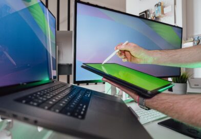 A person using a stylus on a tablet in a tech-savvy workspace with dual monitors