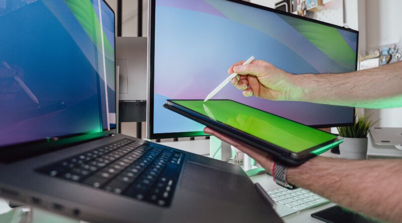 A person using a stylus on a tablet in a tech-savvy workspace with dual monitors