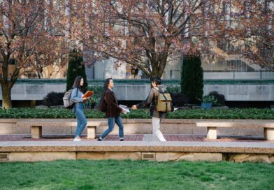 Three students walking and talking at a park during springtime, carrying backpacks.
