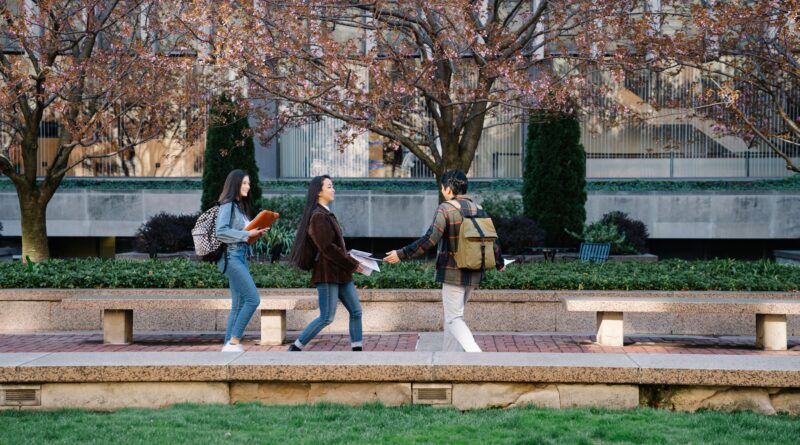 Three students walking and talking at a park during springtime, carrying backpacks.